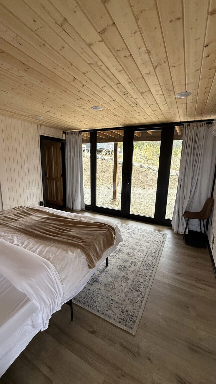 Vertical view of a bedroom with bed facing glass doors inside an Aries 116 cabin in Island Park, ID.