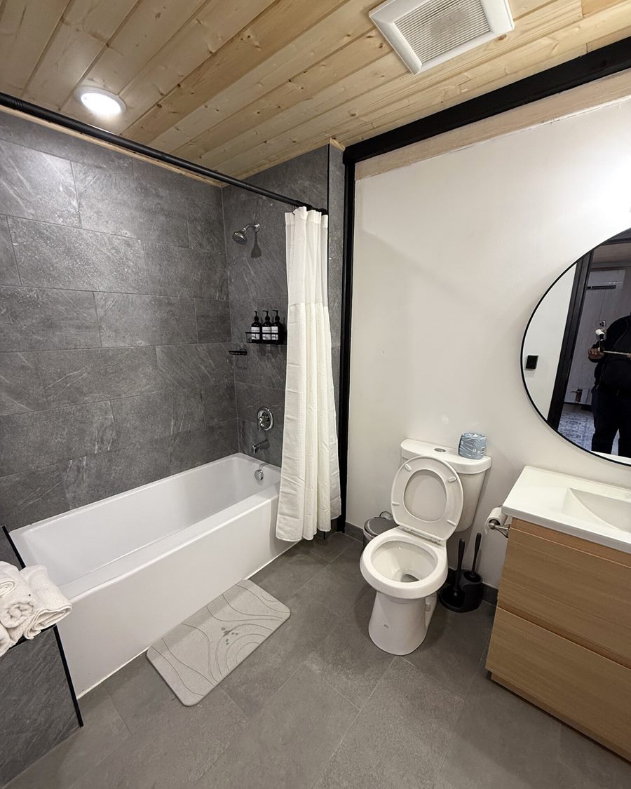 Bathroom with bathtub, toilet, vanity and round mirror inside an Aries 116 cabin in Island Park, ID.
