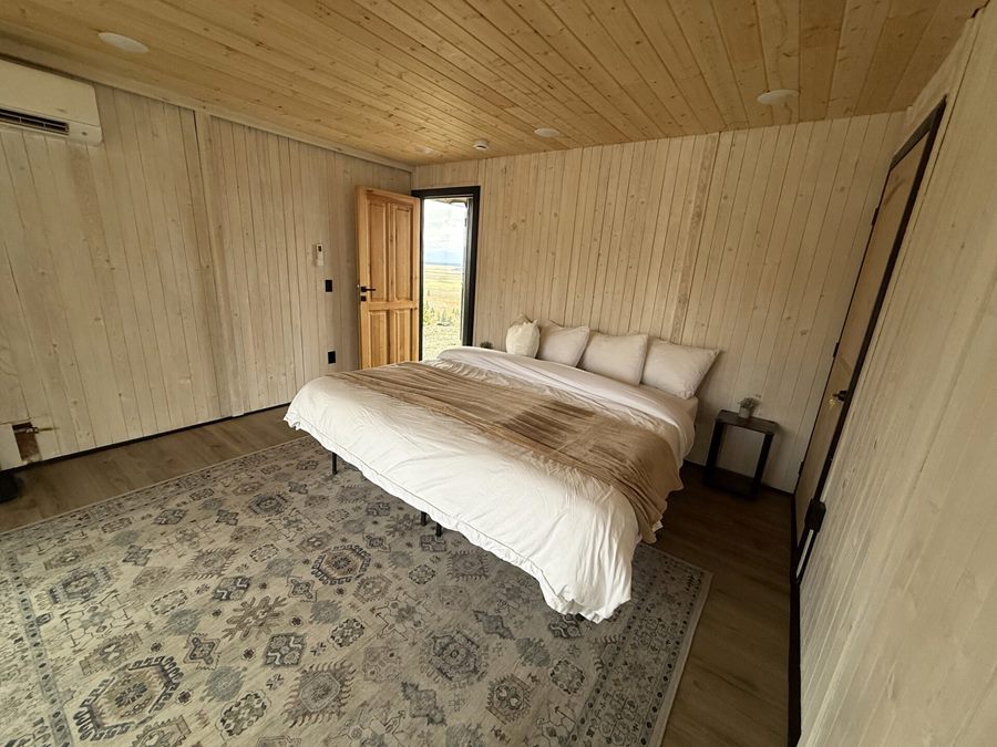 Bedroom with bed, patterned rug and wood-paneled walls inside an Aries 116 cabin in Island Park, ID.