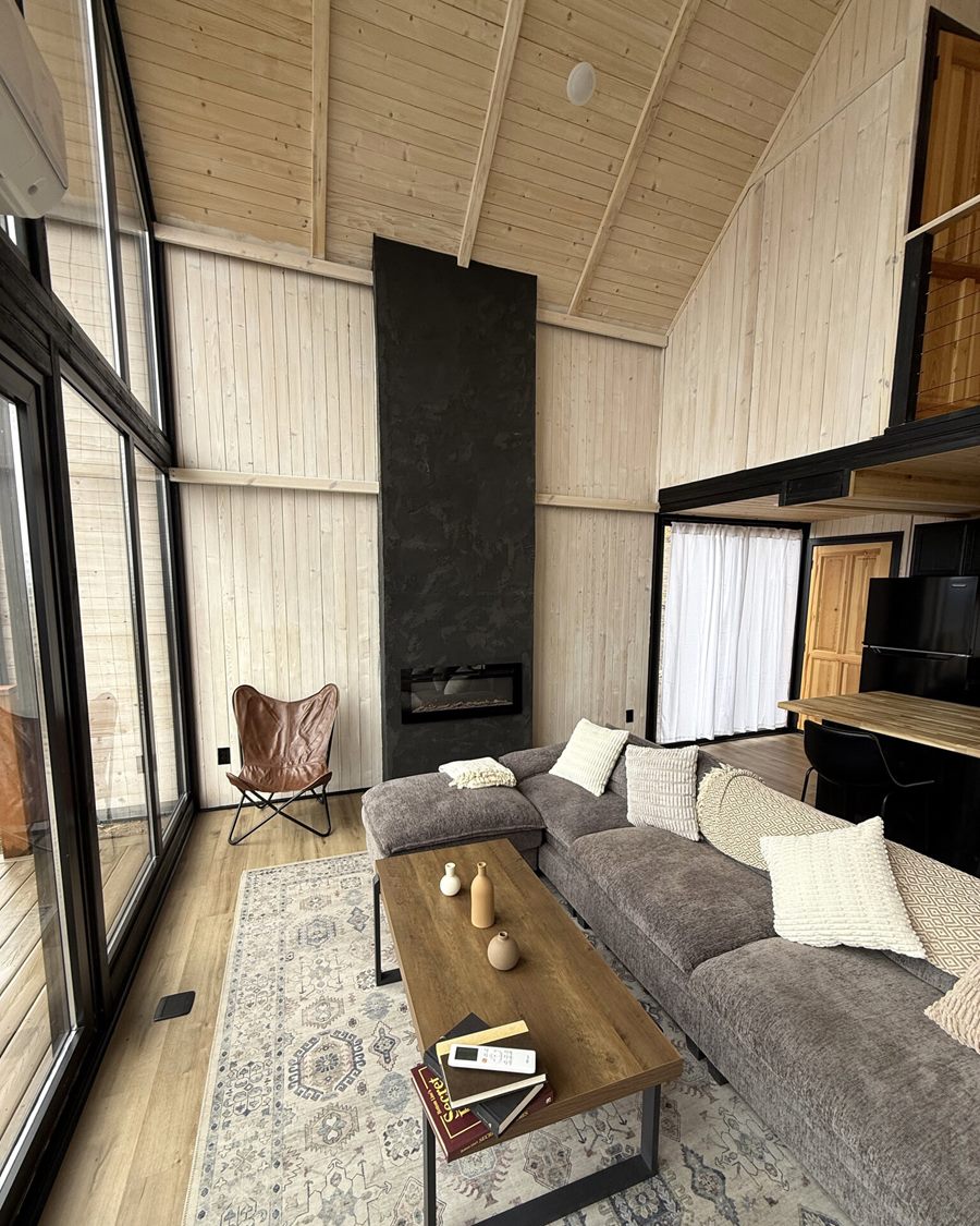 Living area with sectional sofa, wood coffee table and black fireplace inside an Aries 116 cabin in Island Park, ID.