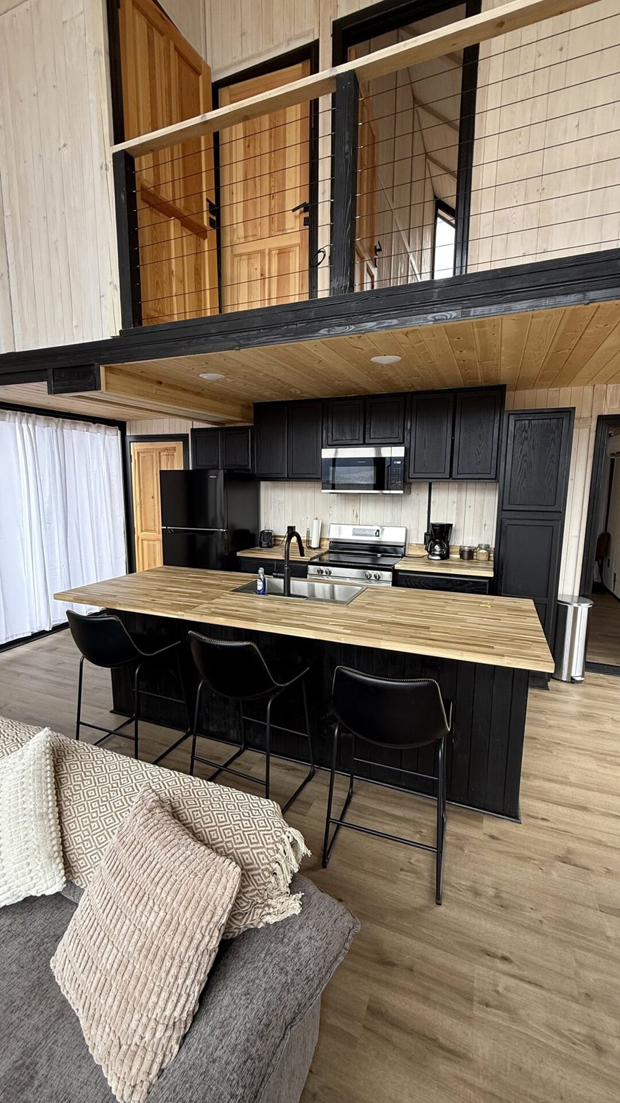 Vertical view of a kitchen with black cabinetry, wood island and bar stools inside an Aries 116 cabin in Island Park, ID.