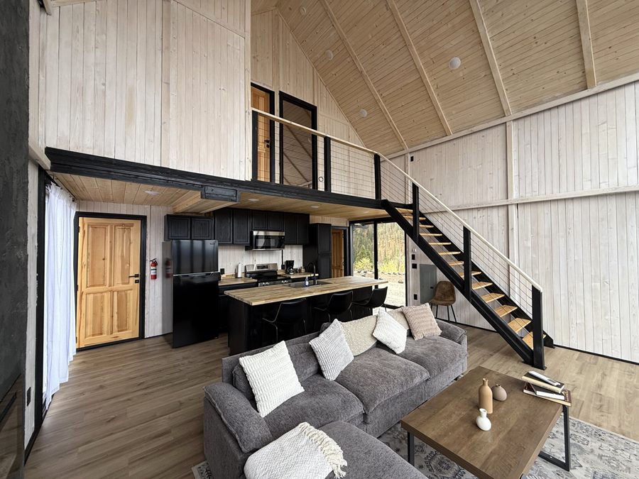 Open living area with sofa, kitchen, staircase and loft inside an Aries 116 cabin in Island Park, ID.