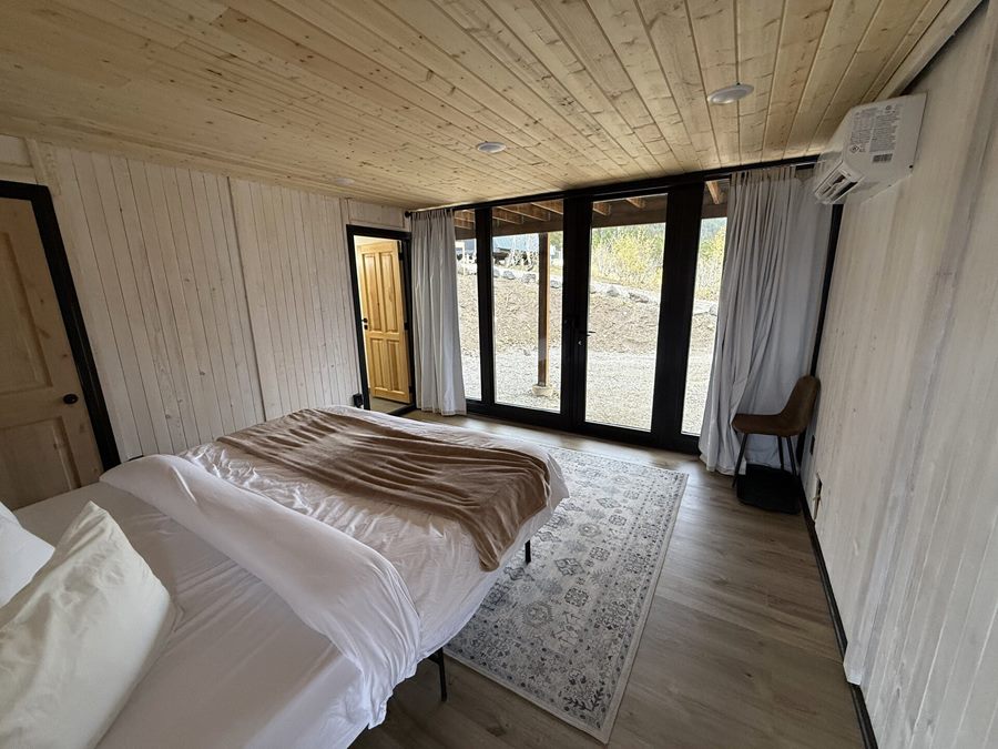 Bedroom with bed facing floor-to-ceiling glass doors inside an Aries 116 cabin in Island Park, ID.