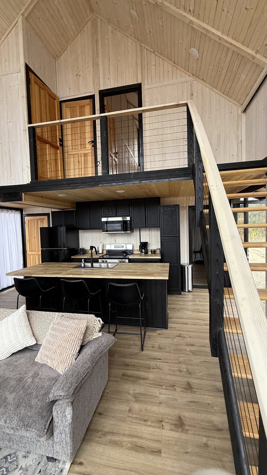 Vertical view of the open kitchen, living area, staircase and loft inside an Aries 116 cabin in Island Park, ID.