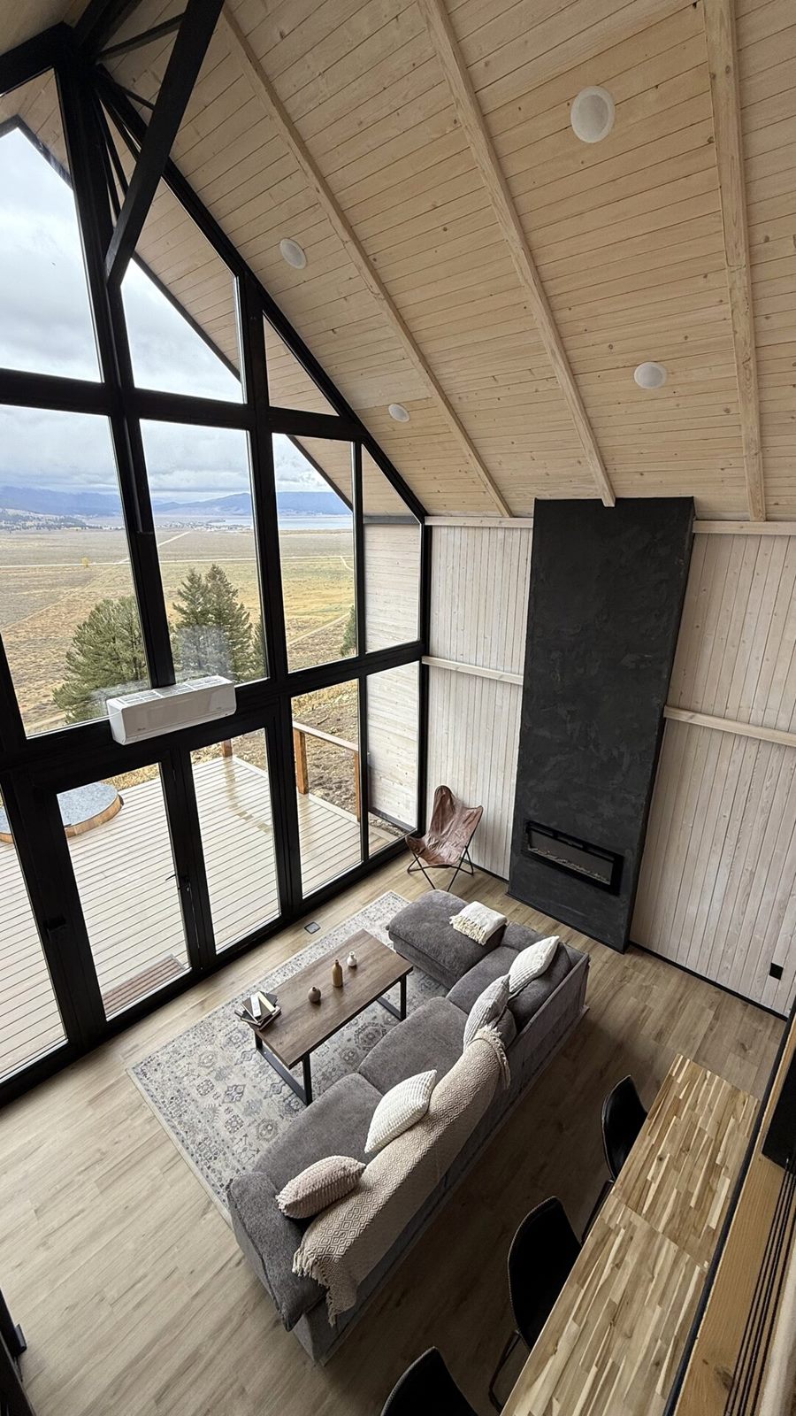 Vertical view from the loft over the sofa and fireplace beside the tall front windows of an Aries 116 cabin in Island Park, ID.