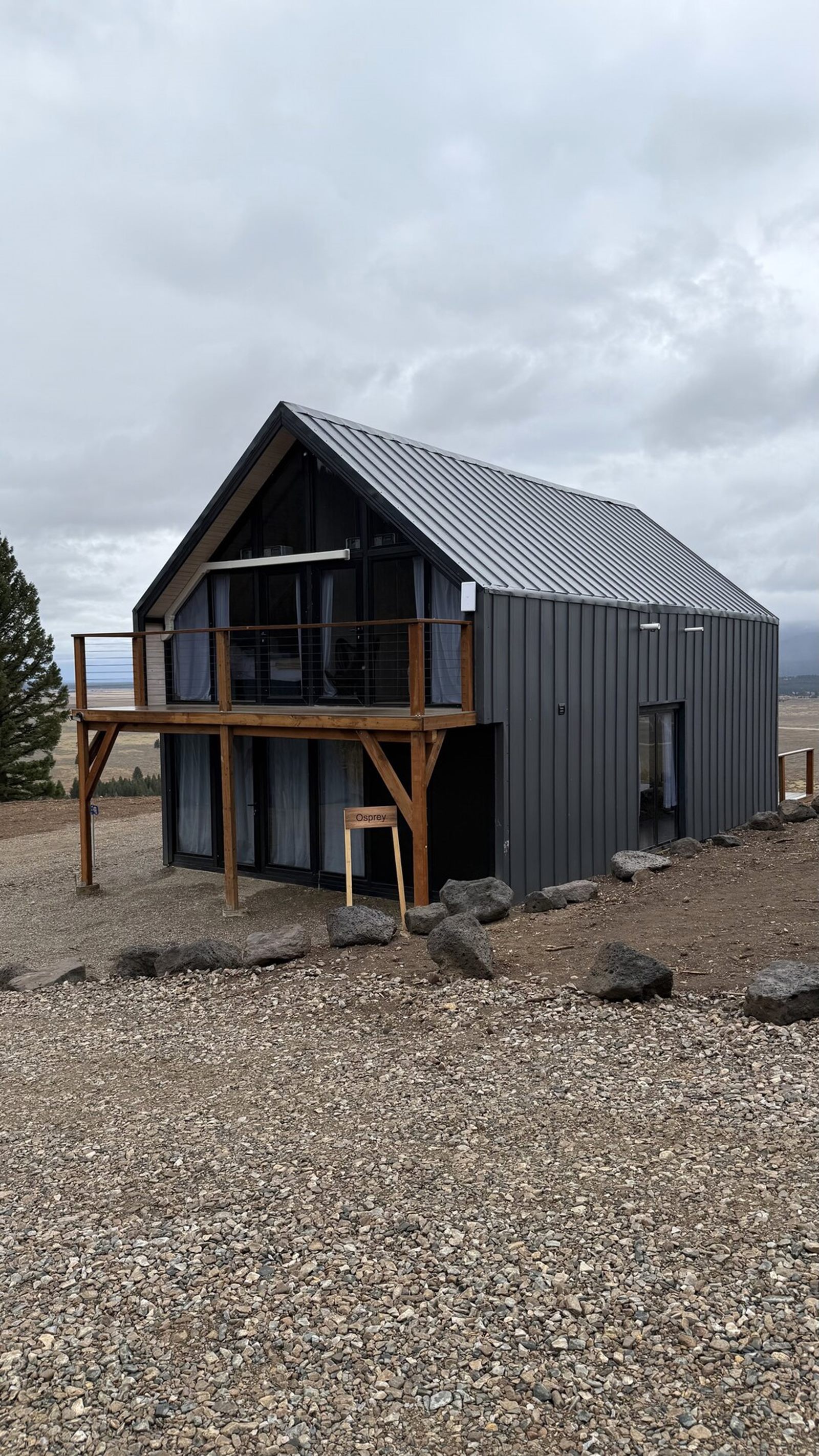 Vertical exterior view of a completed Aries 116 cabin with dark metal cladding and locally built upper balcony in Island Park, ID.