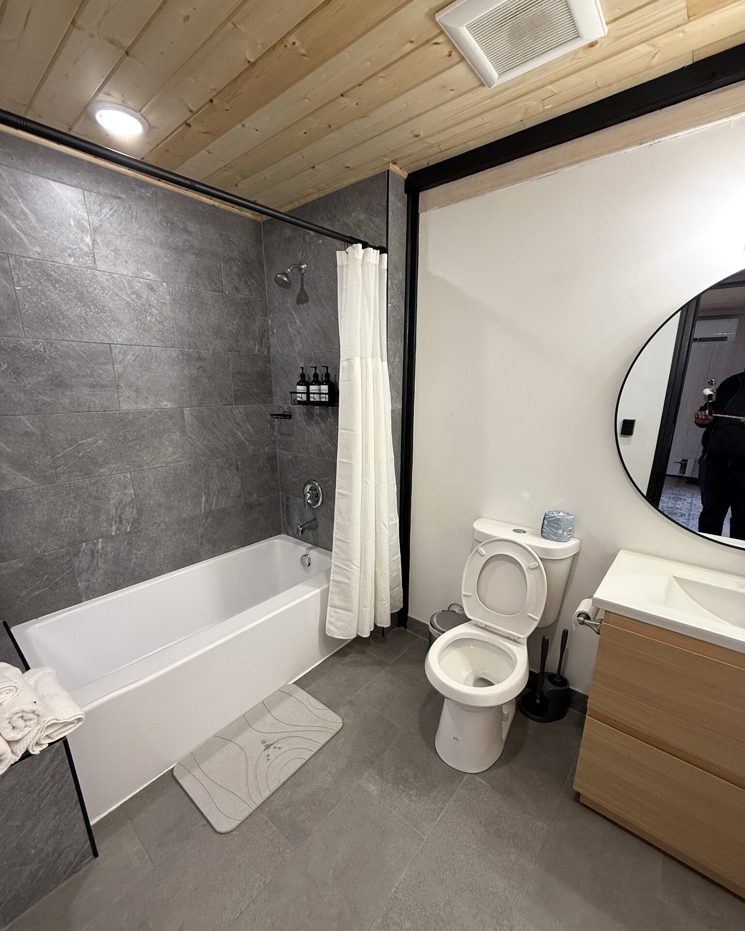 Bathroom with a bathtub, toilet, vanity and round mirror inside an Aries 116 cabin.