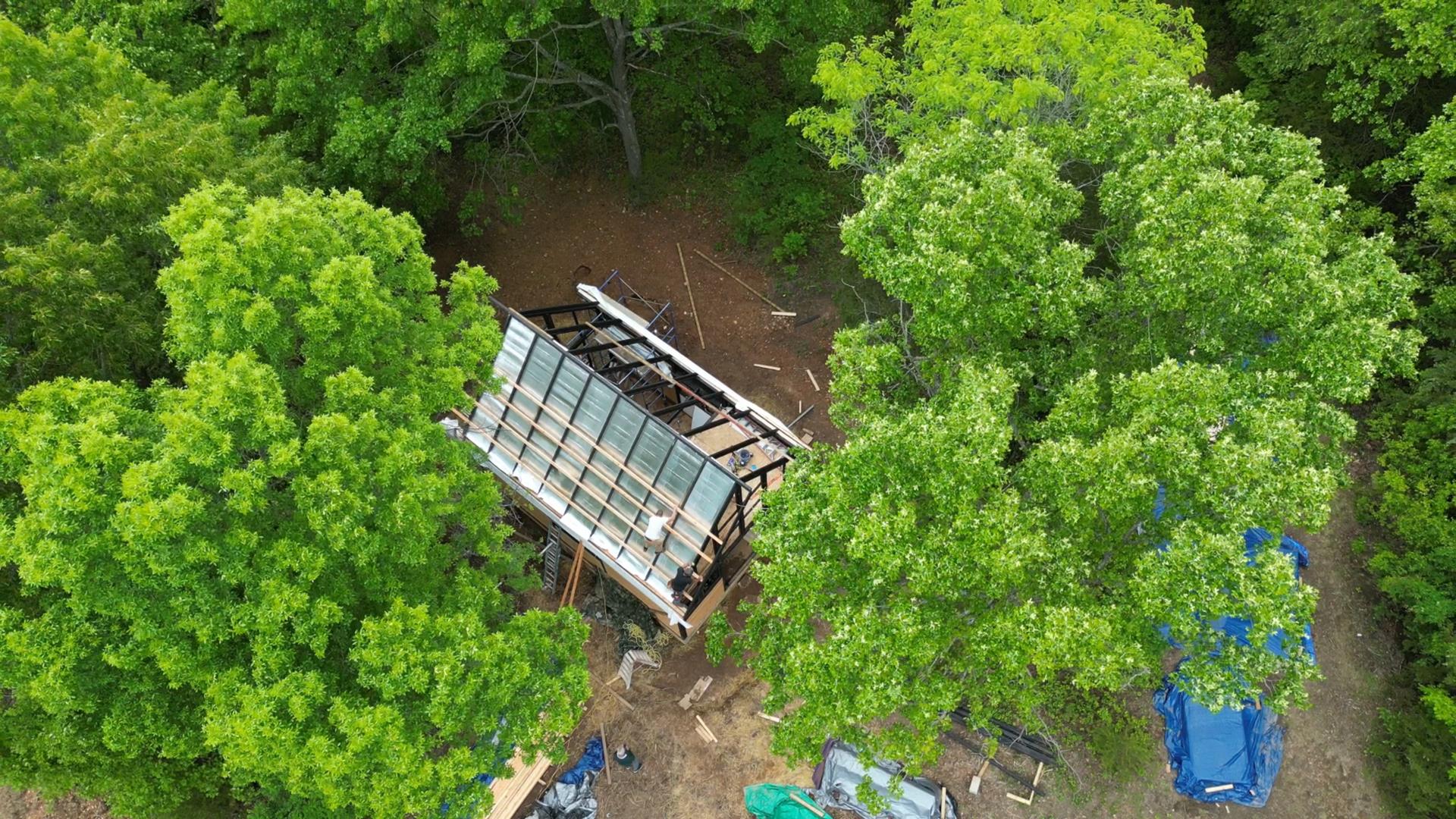 Drone view of the Aries 96 modern A-frame cabin taking shape on a wooded sloped build site in the Arkansas Ozarks.