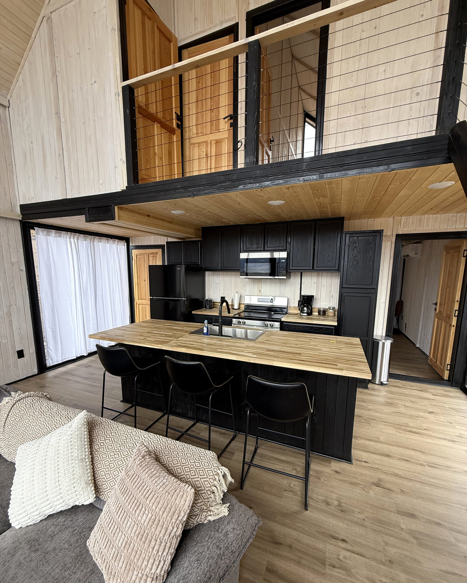 Kitchen with a wood island, black cabinetry and a loft above inside an Aries 116 cabin.