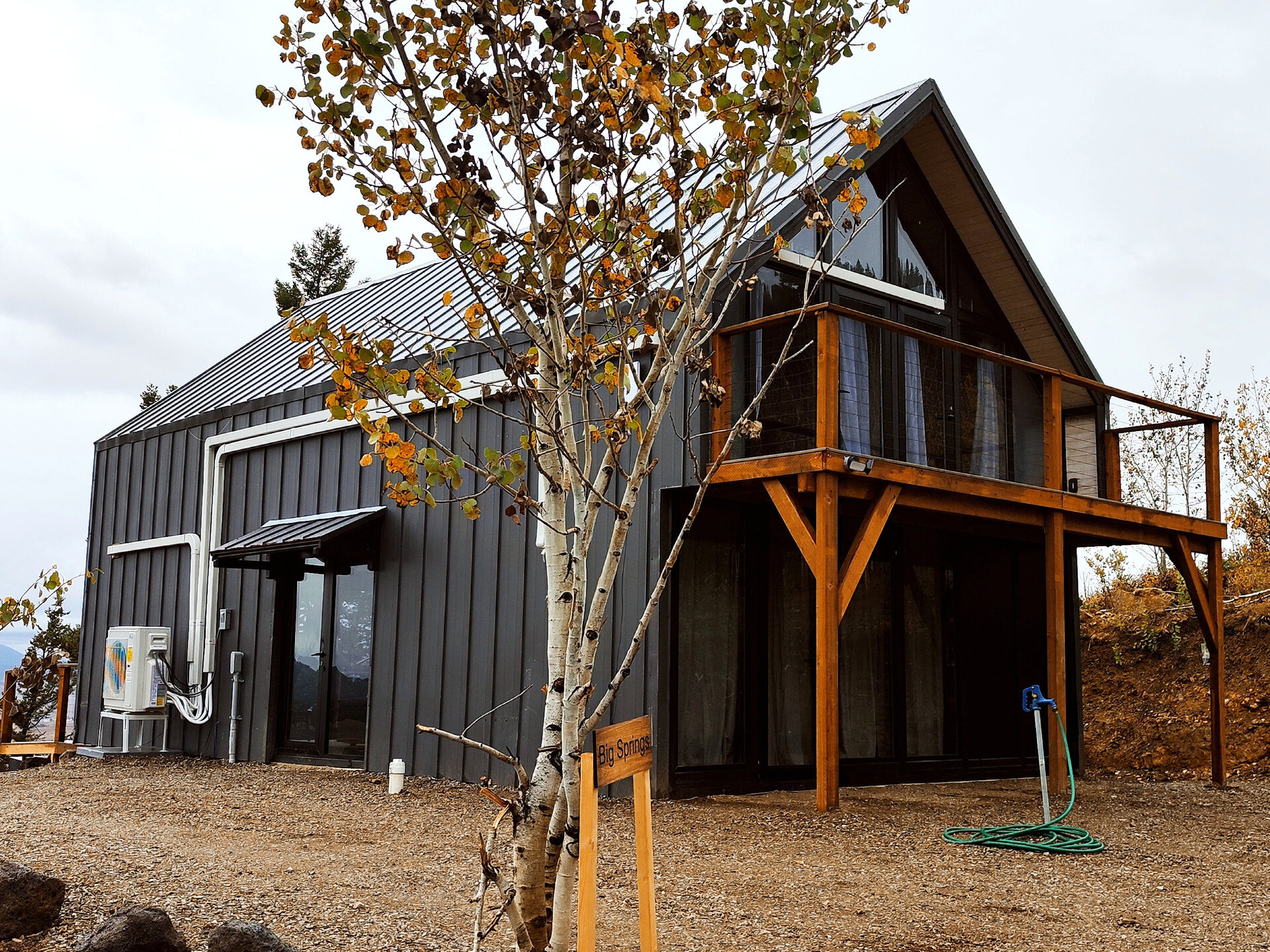 Completed dark-gray Aries 116 cabin with a raised wooden balcony among autumn trees in Island Park, Idaho.