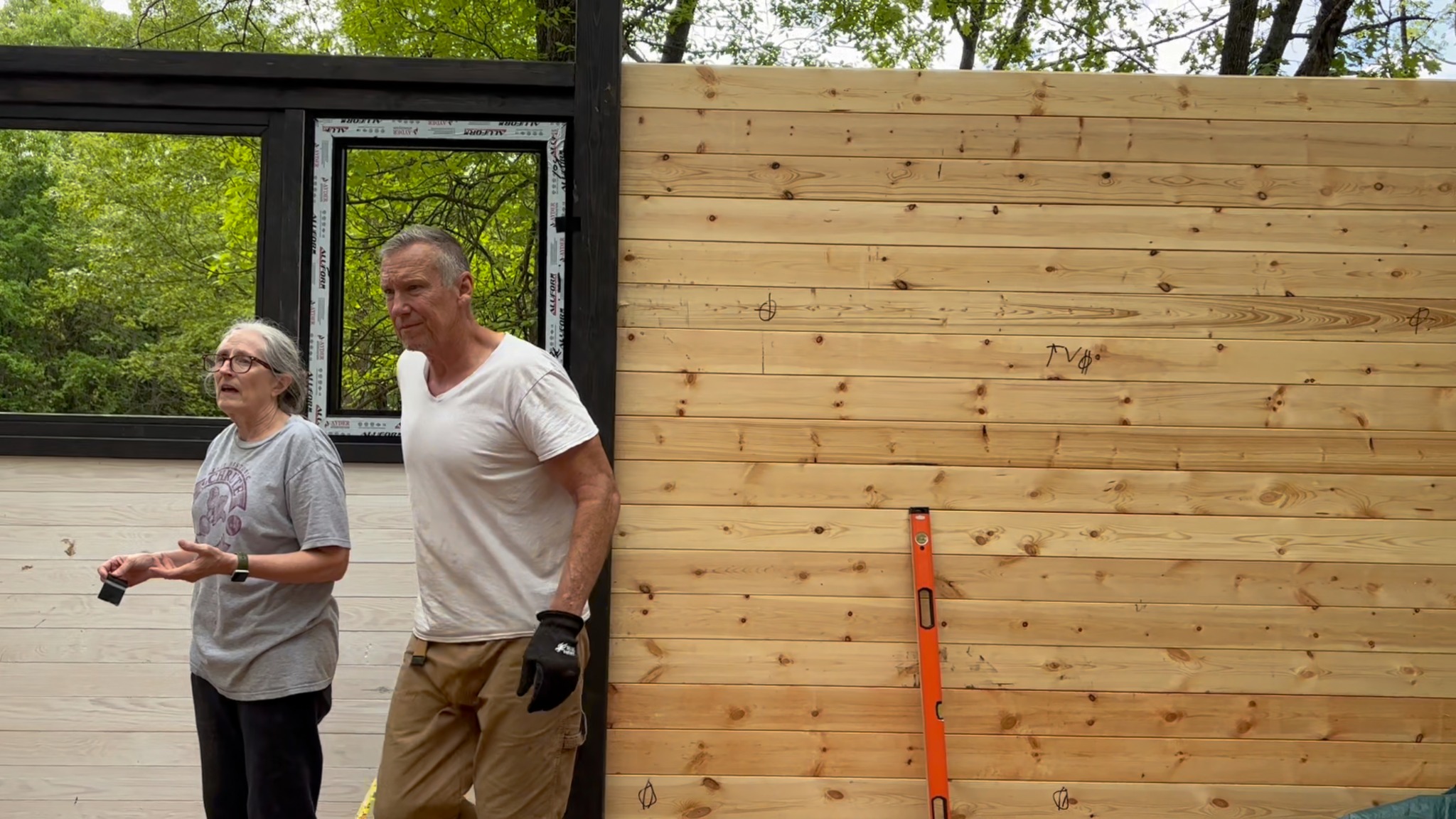Owners beside newly installed timber wall panels and window framing during the Aries 96 cabin build in Omaha, Arkansas.