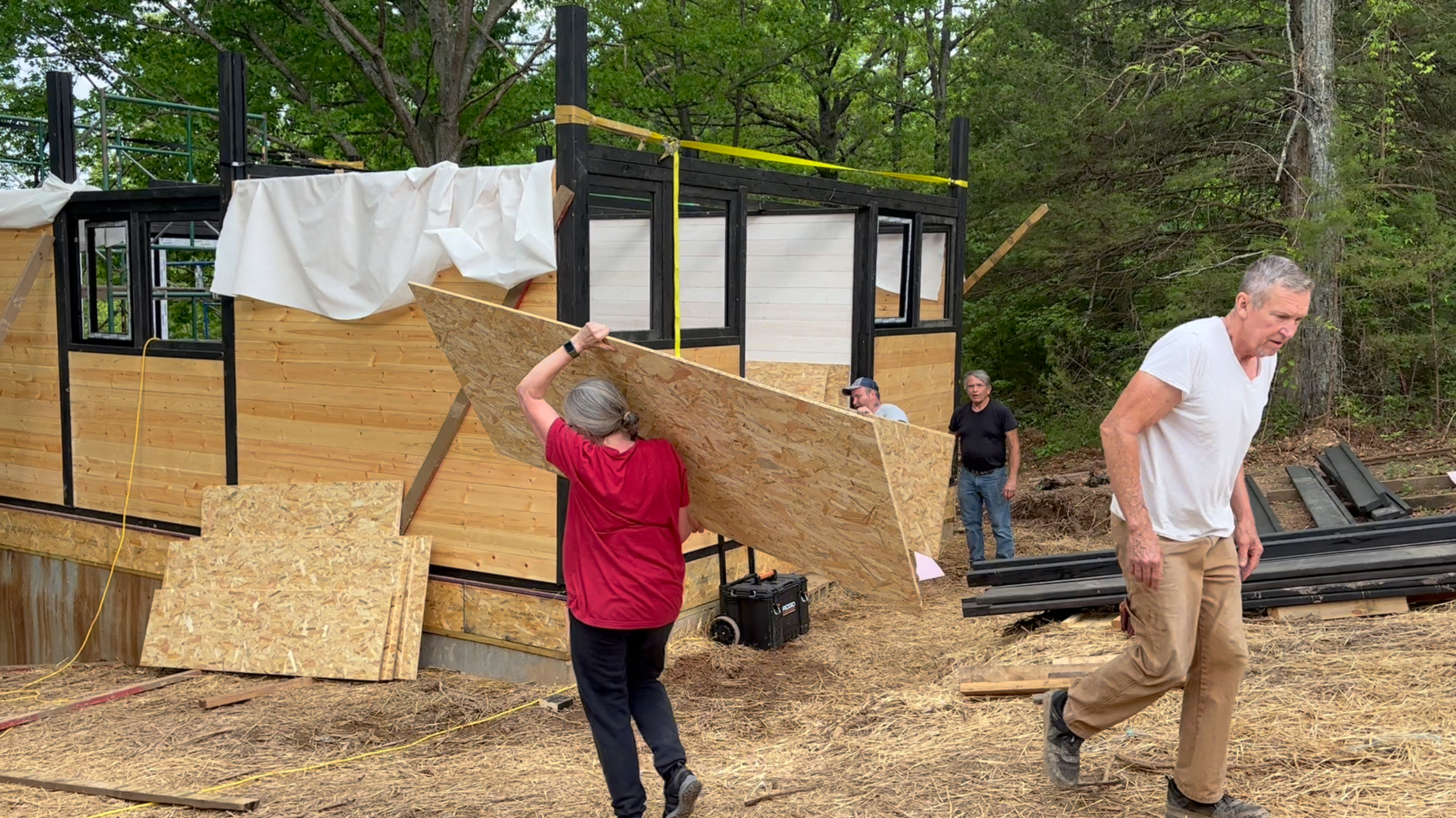 Owners carrying cabin-kit materials to the wooded build site for the Aries 96 project in Omaha, Arkansas.