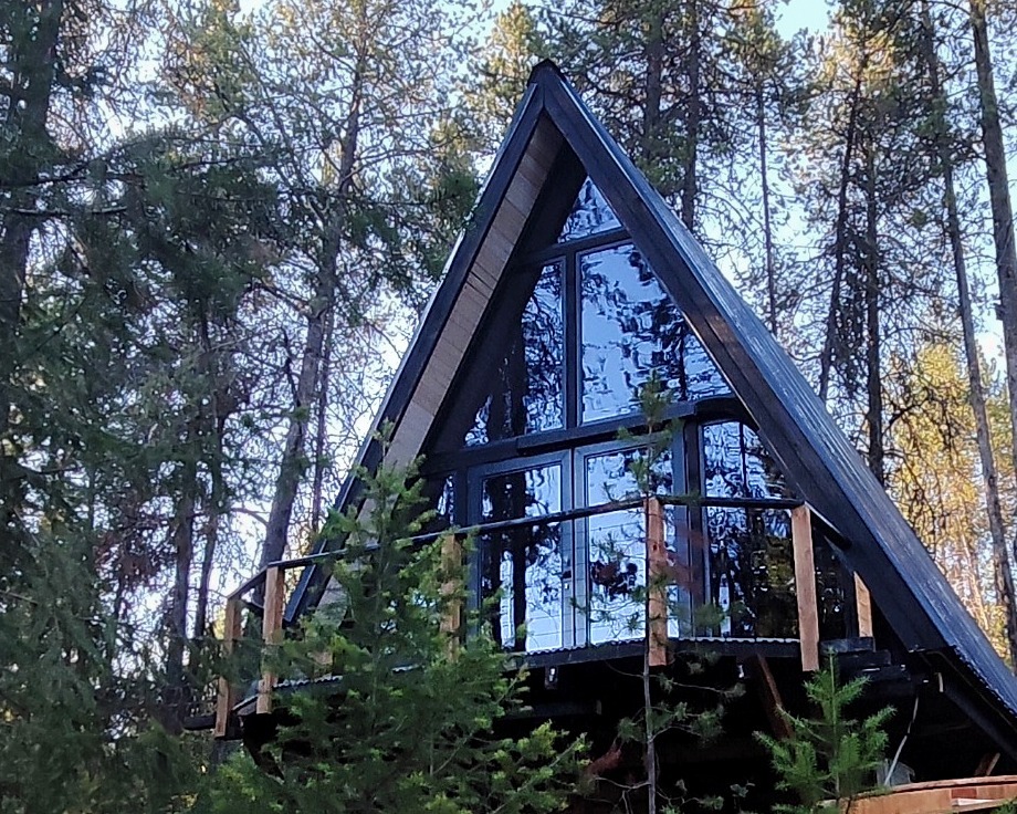 Front view of a Stella 53 A-frame cabin surrounded by pine trees near Glacier National Park, Montana.