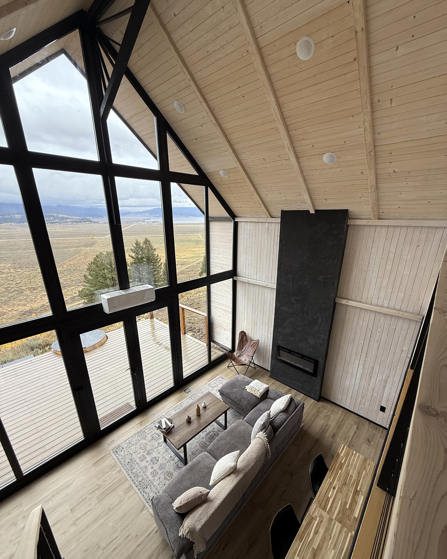 View from the loft over the living area, tall windows and black fireplace inside an Aries 116 cabin.