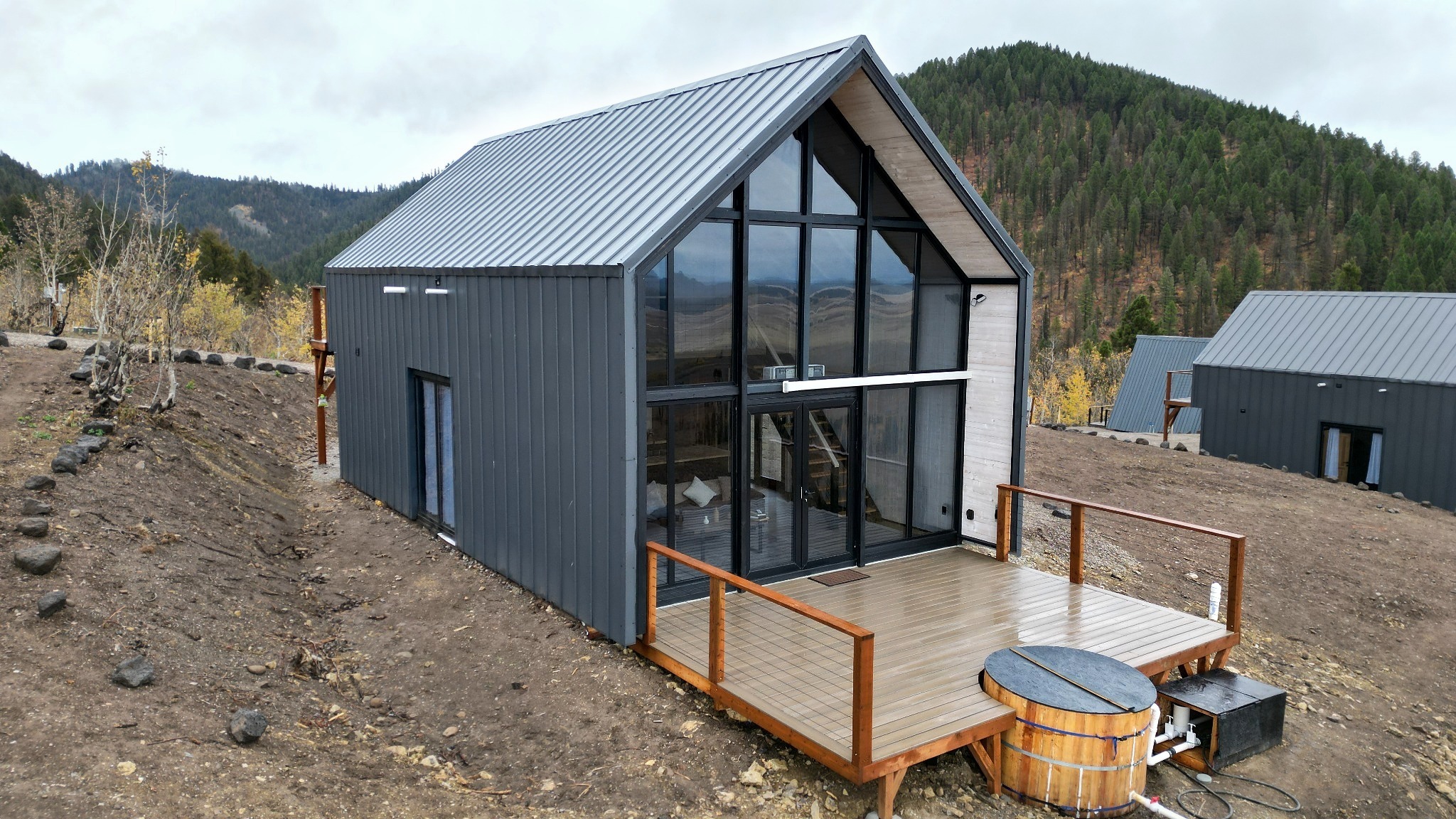 Aries 96 modern cabin with metal cladding, a glazed front façade and a wooden deck in a mountainous forest setting at Island Park Idaho