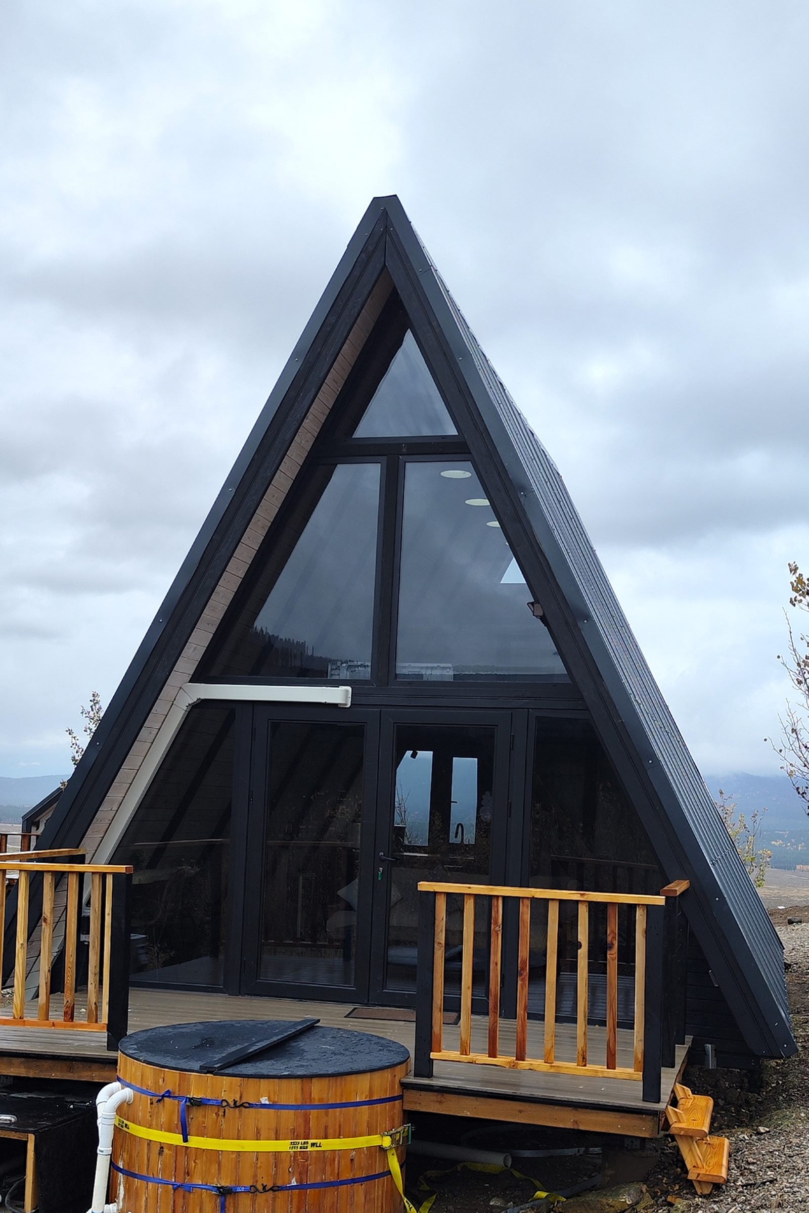 Completed Stella 53 A-frame cabin with a front deck and round hot tub in Island Park, ID.