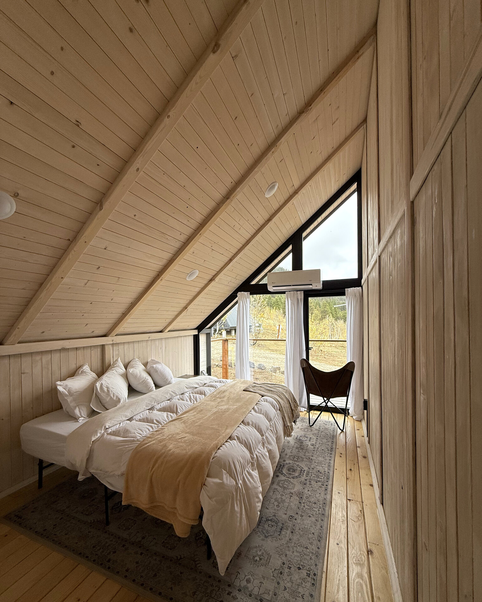 Furnished loft bedroom with a bed, rug and tall triangular window inside an Aries 116 cabin.