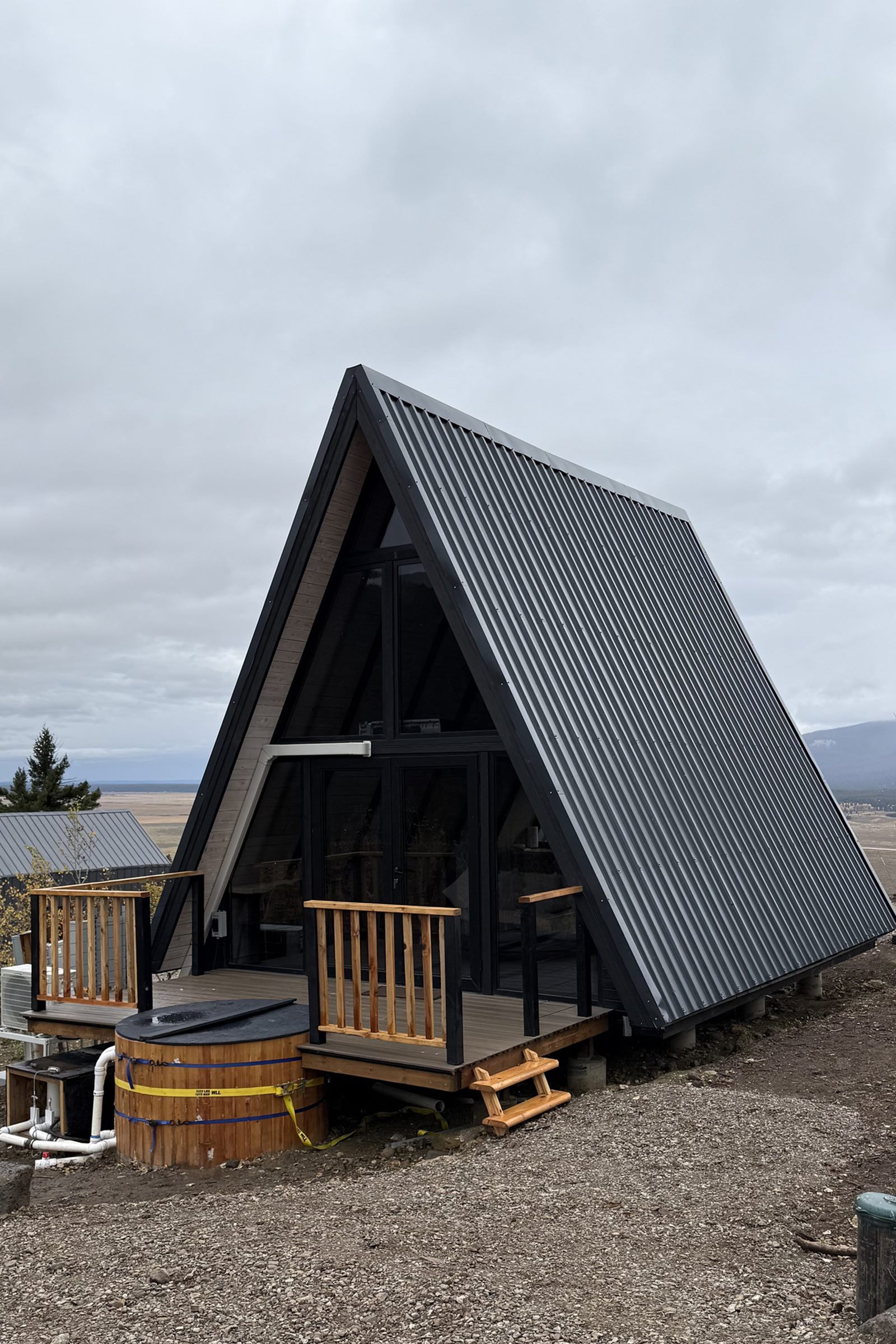 Rear three-quarter view of a completed Stella 53 cabin with a locally built deck and hot tub in Island Park, ID.