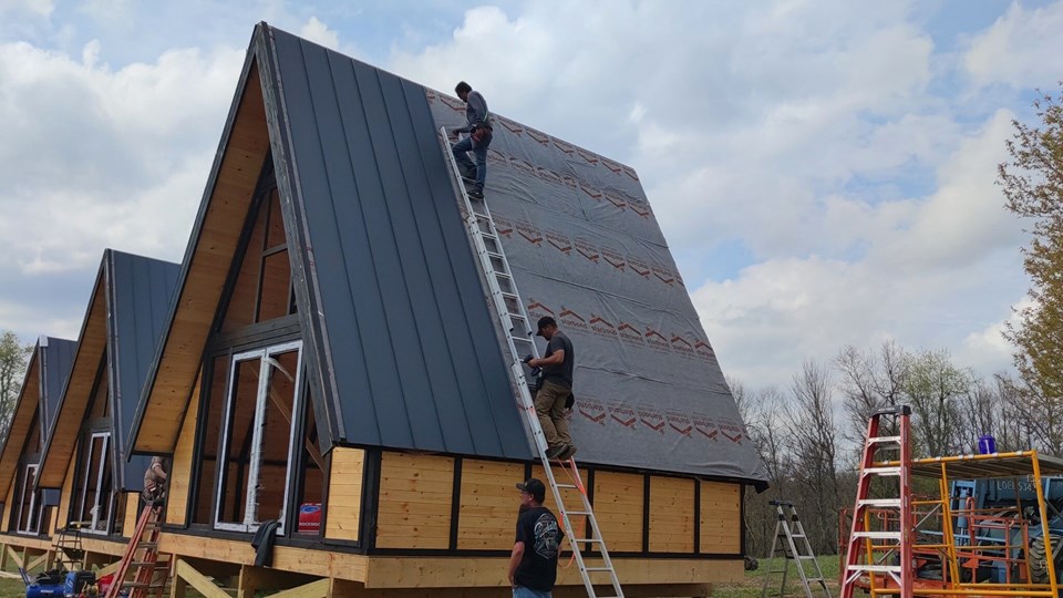 Dark standing-seam metal panels installed progressively across the steep A-frame roof. West Virginia / Earlier configuration.
