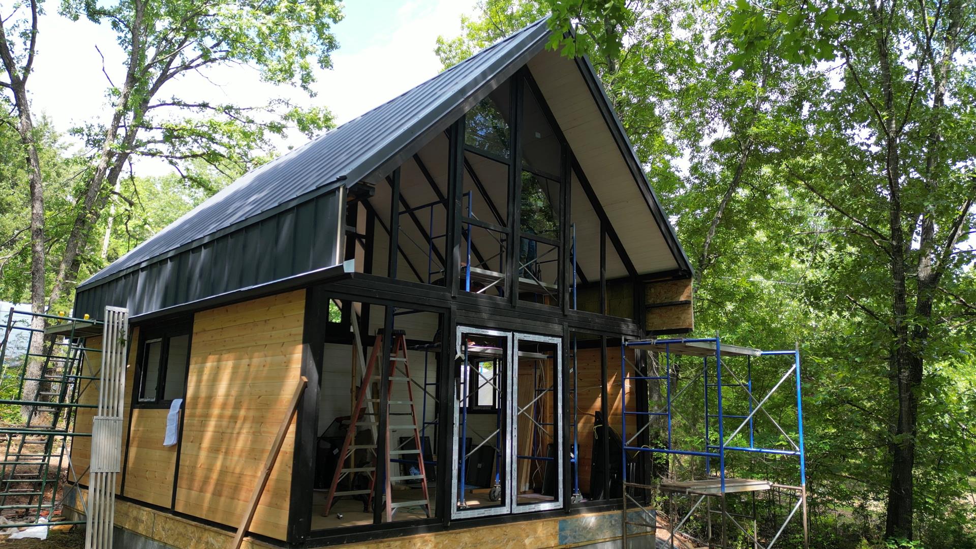 Front exterior view of the Aries 96 modern A-frame cabin showing its black metal roof, tall glass facade, and contemporary form in the Arkansas Ozarks.