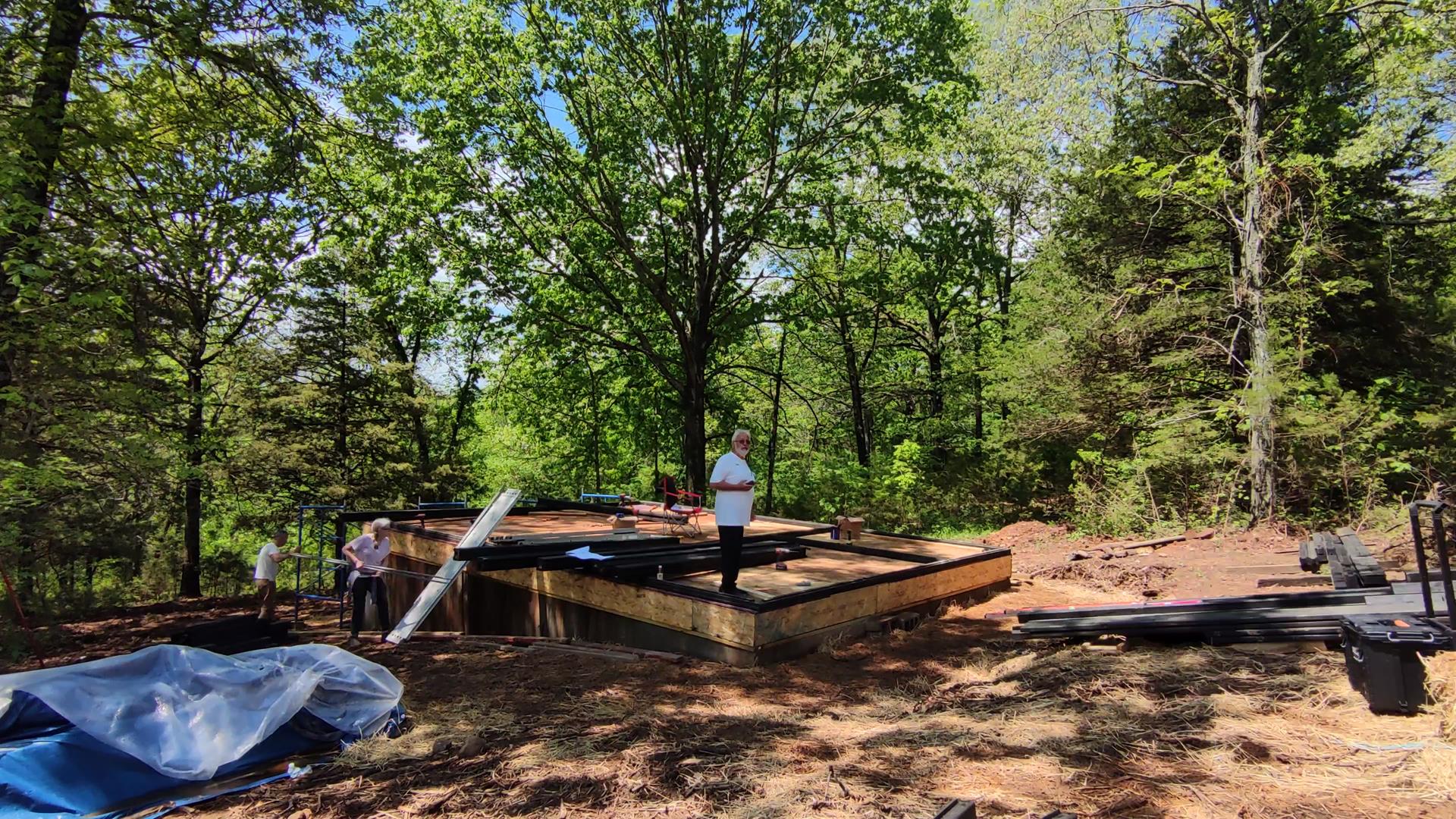 Owners and crew working around the Aries 96 modern A-frame cabin platform on a wooded and challenging Arkansas Ozarks build site.
