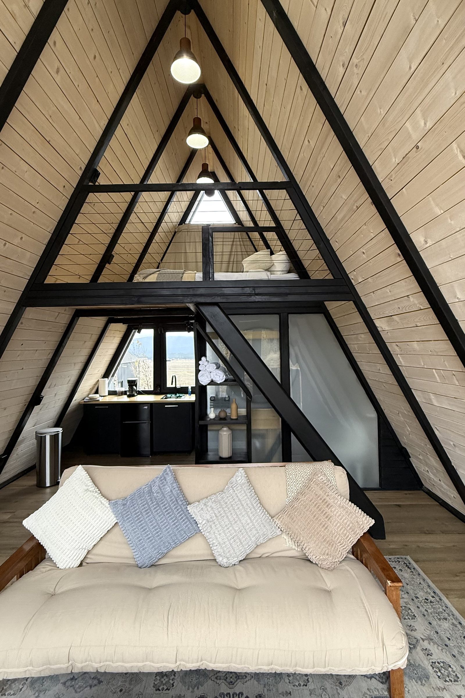 Double-height Stella 53 A-frame cabin interior with sofa, loft and compact kitchen in Island Park, ID.
