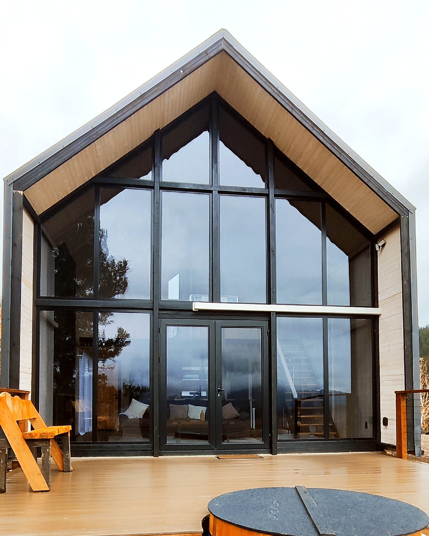 Front glass facade and round wooden hot tub beside the deck of an Aries 116 cabin in Island Park, Idaho.