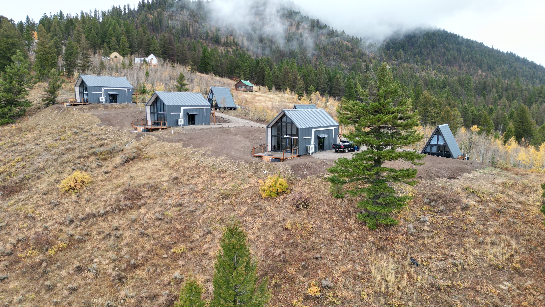 Six completed Aries 116 and Stella 53 rental cabins on a wooded hillside in Island Park, Idaho.
