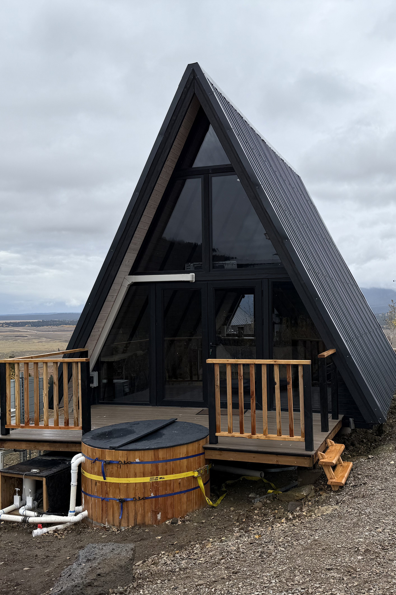 Completed Stella 53 A-frame cabin with timber deck and round hot tub at the Island Park, Idaho hospitality project.