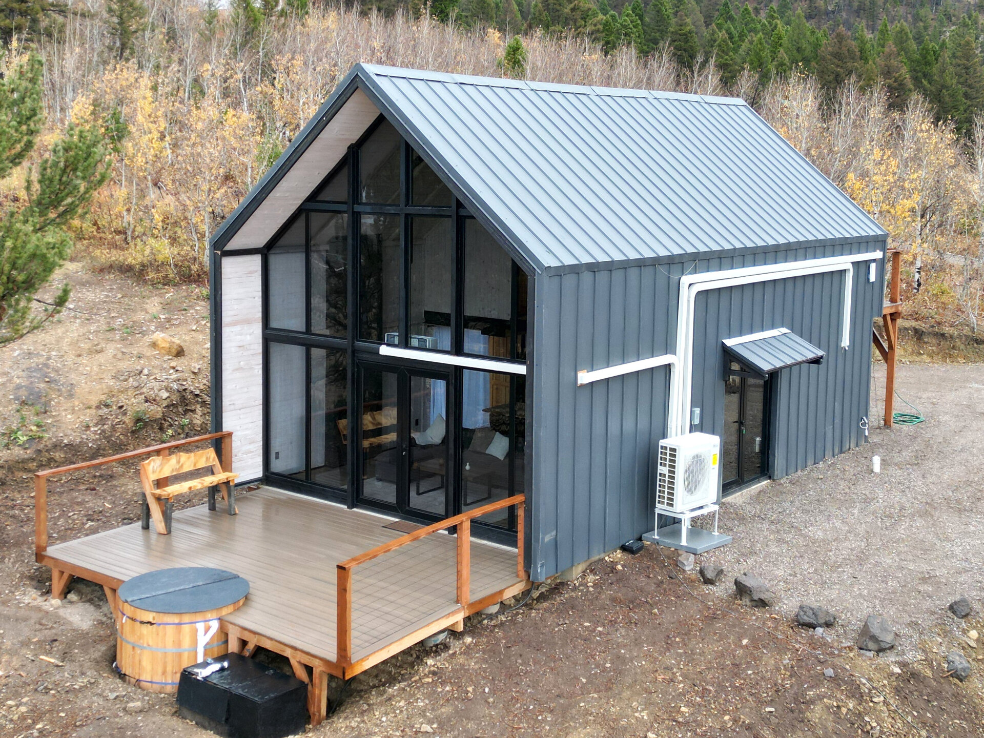 Aerial three-quarter view of a completed Aries 116 cabin with a glass front, deck and hot tub in Island Park, Idaho.