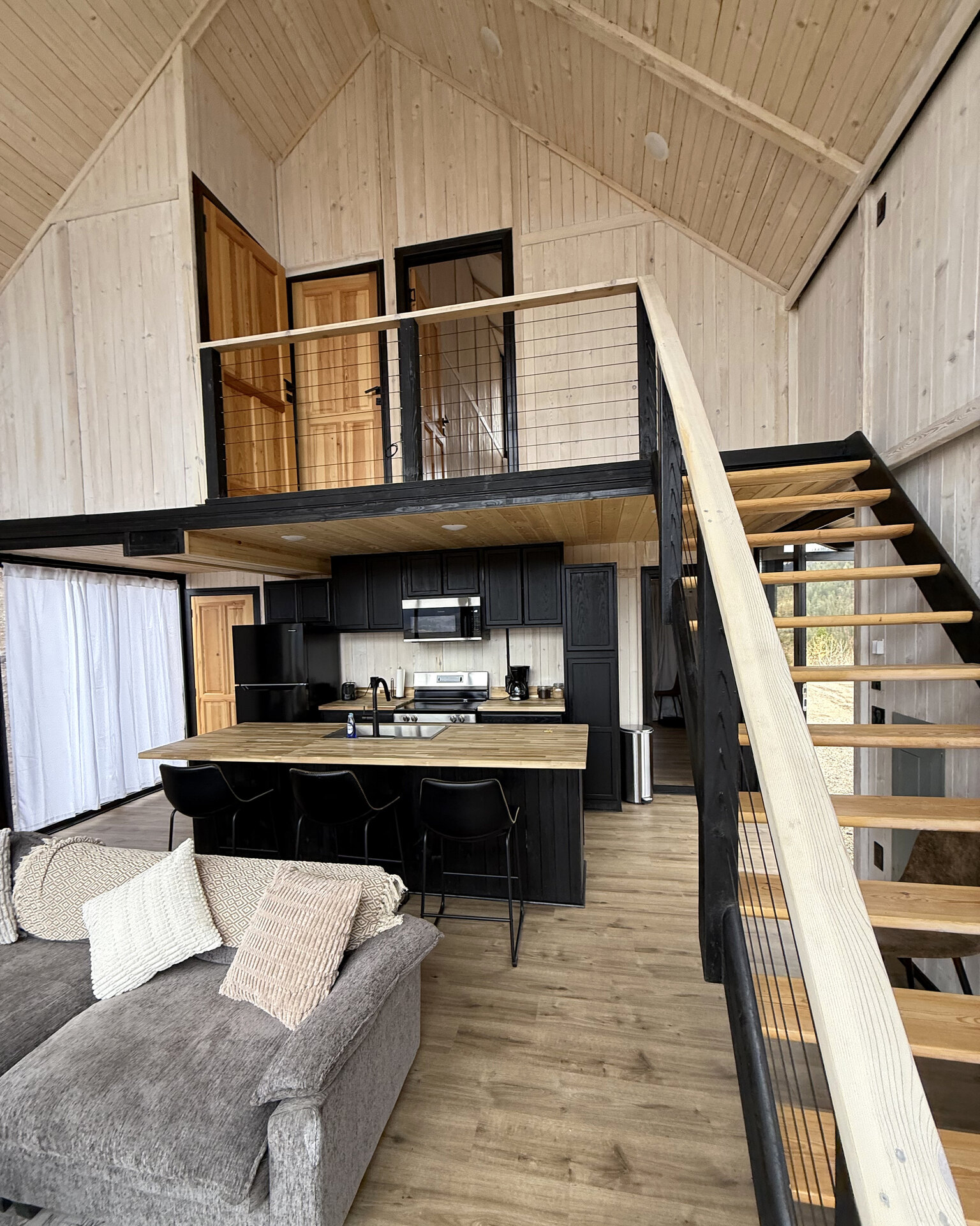 Open-plan living area with a kitchen, staircase and loft railing inside an Aries 116 cabin.