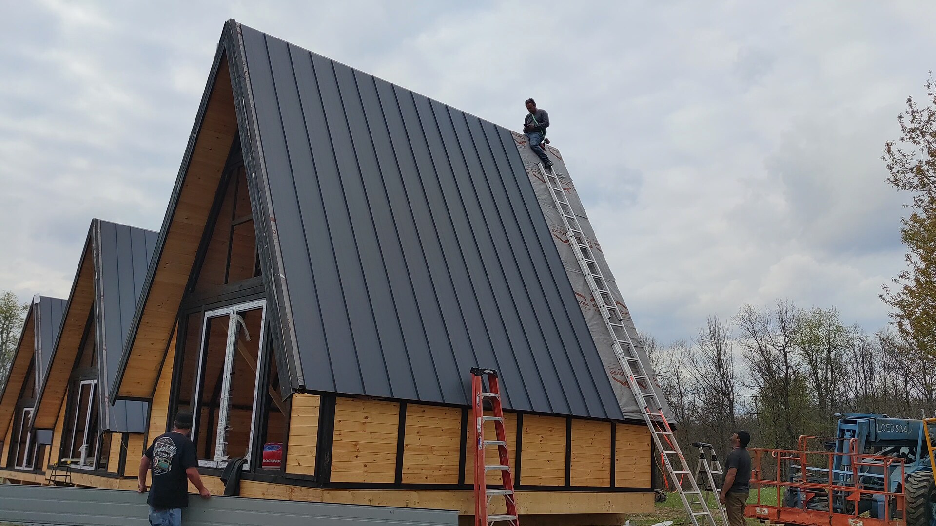 Installer completing the dark standing-seam metal roof on a Stella 70 cabin in West Virginia